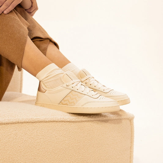 Nachhaltige Sneaker aus beigem Leder mit goldfarbenem Ethno-Muster und weißer Sohle – handgefertigt in Vietnam.